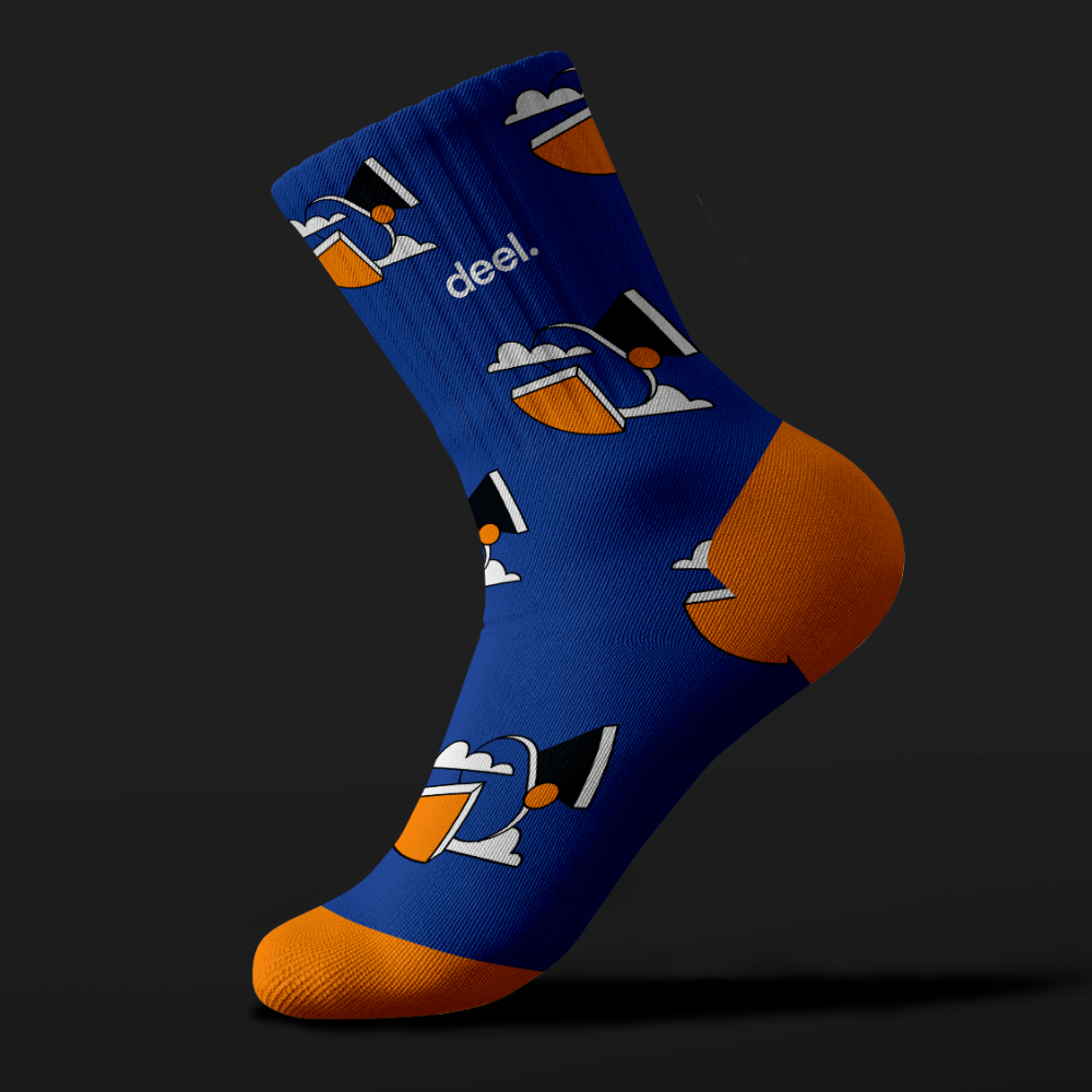 Design As A Subscription 24 Blue sock with an orange heel and toe, featuring a cartoon graphic of a person with a hat and sunglasses against a dark background. The word deel. is printed near the top, showcasing unlimited graphic design creativity.