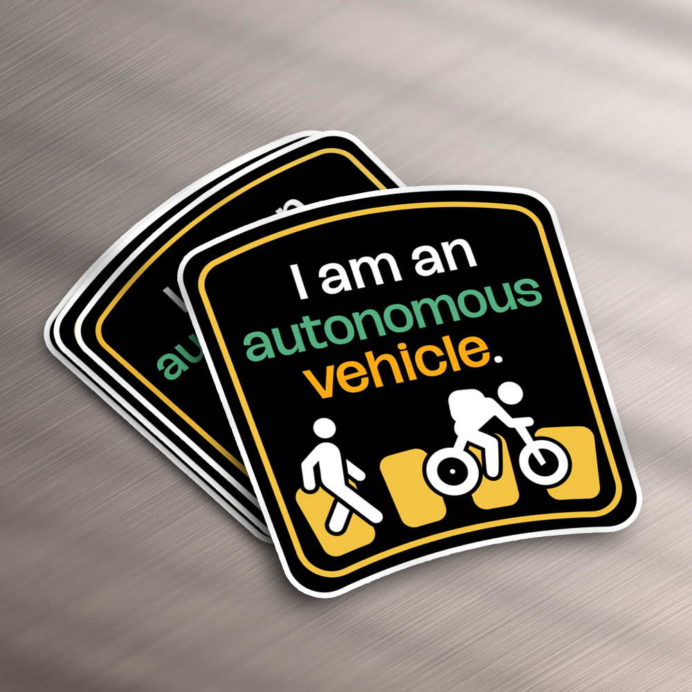 Design As A Subscription 16 These stickers, perfect for a design subscription, flaunt a traffic-themed motif with I am an autonomous vehicle in white, green, and orange. Below this text, icons depict a pedestrian, cyclist, and car against a black backdrop framed in white.